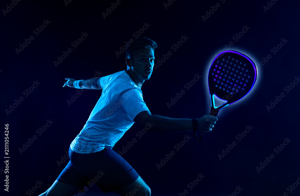 Fototapeta premium Padel tennis player with racket. Man athlete with paddle racket on court with neon colors. Sport concept. Download a high quality photo for the design of a sports app or betting site.
