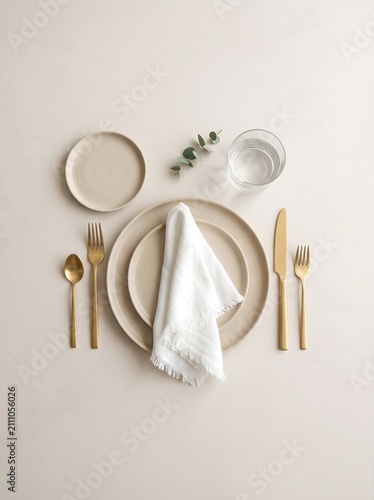Elegant Modern Table Setting with Neutral Tones, Gold Cutlery, and Eucalyptus Sprig on Beige Background