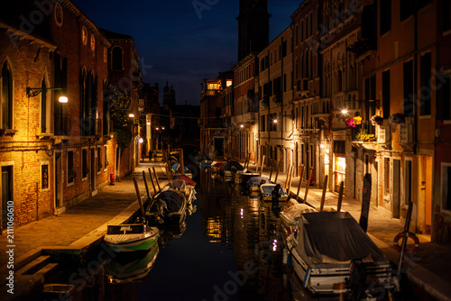 Venice canal with historical buildings and moored boats at night