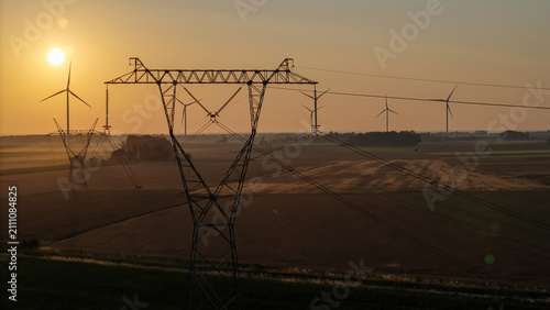High-voltage power lines and wind turbines in rural landscape at morning, renewable energy transformation.