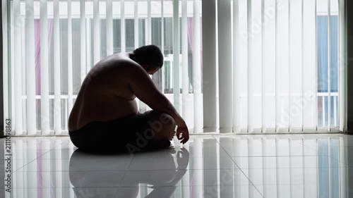 Sad Overweight Man Sitting Cross Legged and Slouching Near Window at Home
