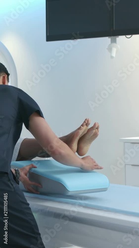 Vertical video: Starting prep, tech scrubs placing blue leg wedge under patient legs on exam table