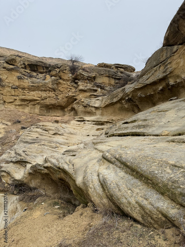 Eroded sandstone cliff with layered formations and sparse vegetation.