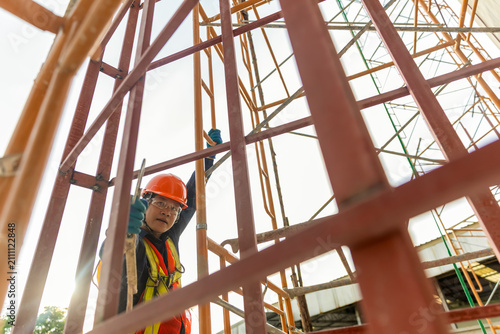 Construction Worker Amidst Steel Frame A construction worker in safety gear, including a hard hat and vest, is positioned within the intricate lattice of a building's steel framework.