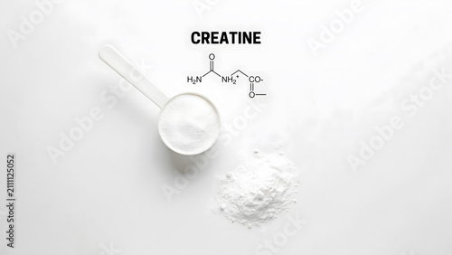 White creatine powder with a plastic measuring scoop on a plain surface