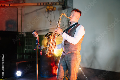 Cuadro en lienzo Solo musician in a formal vest and dress shirt plays a golden saxophone under gl