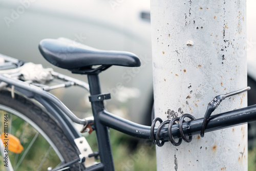 Картината върху платно Bicycle secured with a coiled cable combination lock wrapped around its frame and a metal pole in an urban setting
