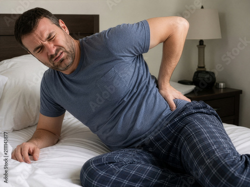 Man with back pain getting into bed