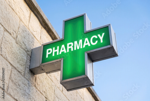 Illuminated Green Pharmacy Cross Sign Against Blue Sky
