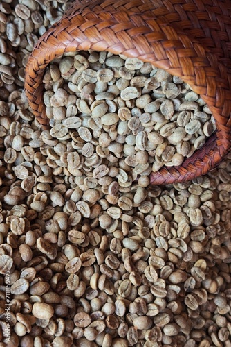  Raw unroasted green coffee beans being poured into a traditional wooden hopper during the specialty coffee processing and roasting workflow.