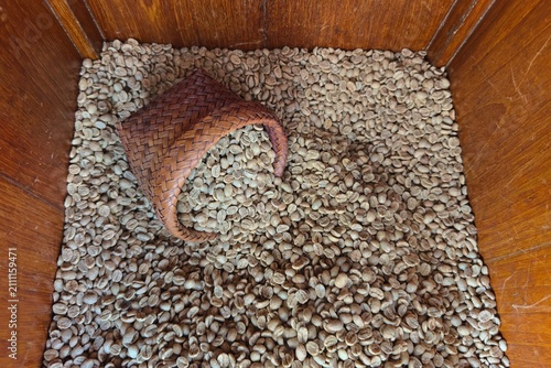  Raw unroasted green coffee beans being poured into a traditional wooden hopper during the specialty coffee processing and roasting workflow.