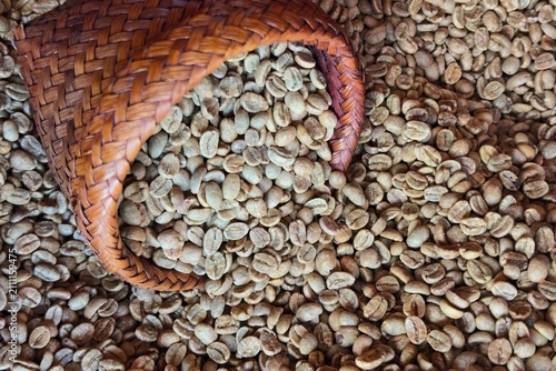  Raw unroasted green coffee beans being poured into a traditional wooden hopper during the specialty coffee processing and roasting workflow.