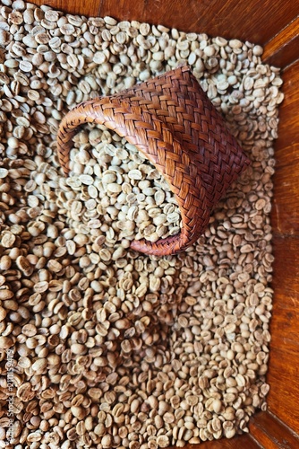  Raw unroasted green coffee beans being poured into a traditional wooden hopper during the specialty coffee processing and roasting workflow.