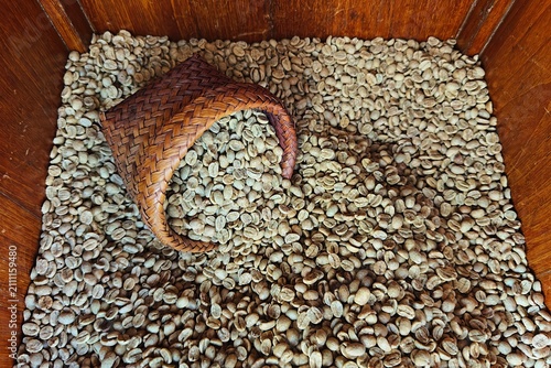  Raw unroasted green coffee beans being poured into a traditional wooden hopper during the specialty coffee processing and roasting workflow.