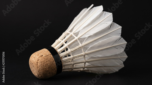 Single white feather shuttlecock lying on a dark background.