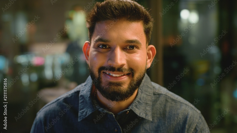 Fototapeta premium Extreme close up portrait Indian business man smiling looking at camera in office company in evening. Headshot ethnic businessman male employer guy specialist startup leader smile positive candid