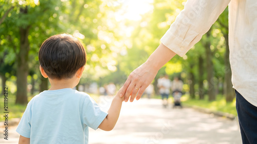 新緑の公園でしっかりと手をつないで散歩する親子の後ろ姿の手元
