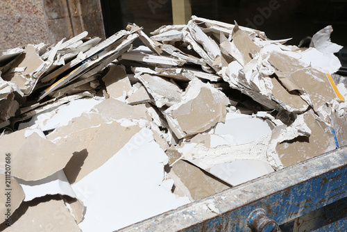 Broken drywall and plaster rubble background. Construction waste inside metal dumpster. Demolition debris ready for recycling and renovation cleanup. Building materials after interior remodeling.