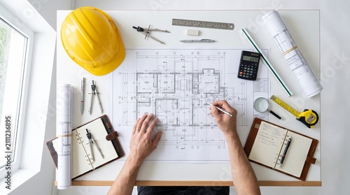 Architectural team reviewing residential floor plans with construction drawings and engineering equipment on office desk
