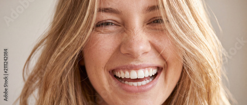 Close up portrait of laughing blonde woman featuring genuine smile, soft natural lighting, and warm beige tones for skincare, dental health, beauty care, and wellness visual advertising