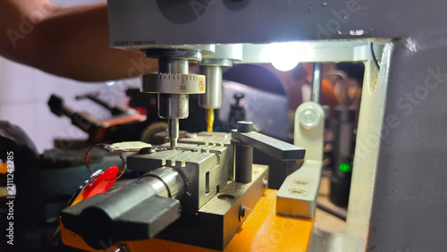 Obraz na plátne Close-up of a locksmith duplicating an original metal key, precisely milling matching grooves into a new key blank with selective focus, highlighting professional security and replacement services