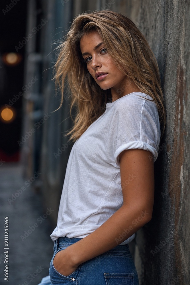 Fototapeta premium Fashion model posing against a textured wall with dramatic urban ambiance.