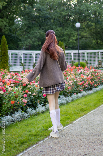 Teenage girl walks along a path through a blooming rose garden on a warm summer evening. Concept of independence, confidence, peaceful leisure and everyday outdoor lifestyle.