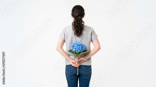 Rear view of a person hiding a vibrant blue hydrangea flower behind their back.