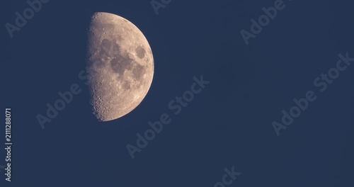 First quarter moon rising through dark blue twilight clouds time lapse