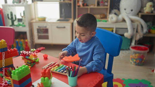 Bild auf Leinwand Hispanic boy holds mallet, striking a colorful xylophone and tapping keys with his hand in a playroom building; concentration