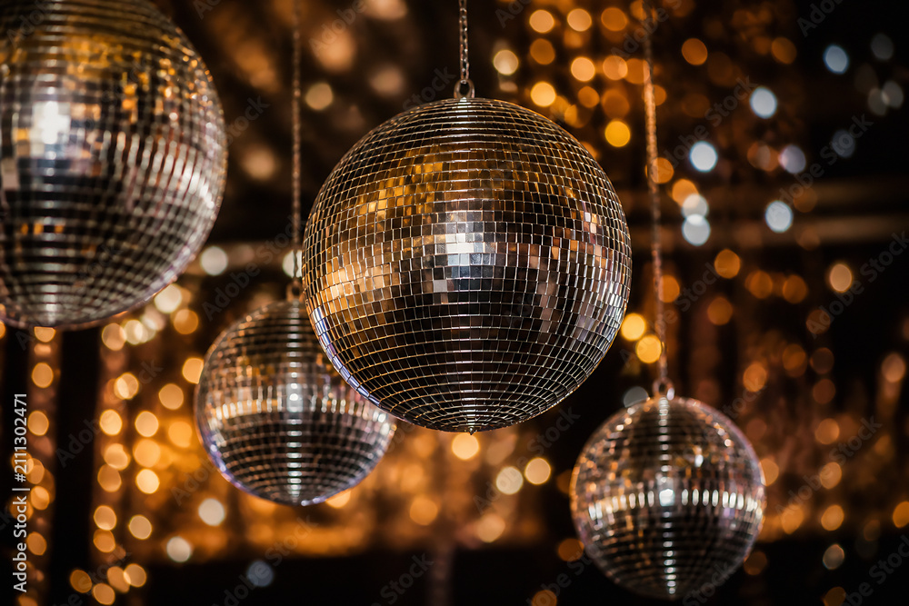 Obraz premium Multiple disco balls hang in a dimly lit, sparkling party or club setting.