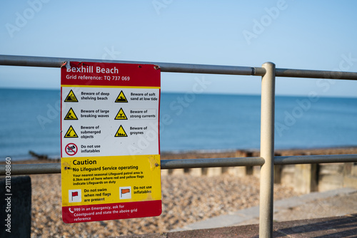 Konstfotografi Beach hazard information sign at Bexhill Beach beside a seaside promenade