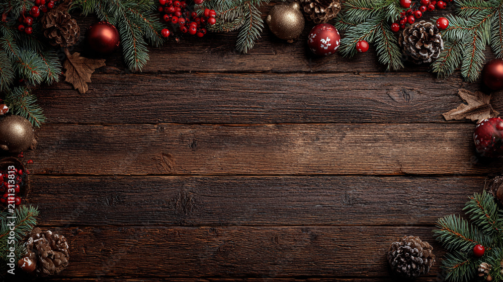 Obraz premium Festive Christmas background on dark wood featuring pine branches, cones, candy canes, red berries, angel wings, and gifts at top with copy space.