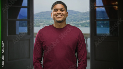 фотографія Man with beard smiling in a building doorway on a balcony overlooking a lake and mountains; contentment calm presence