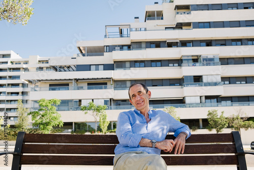 Senior man smiling on bench near luxury apartments in summer