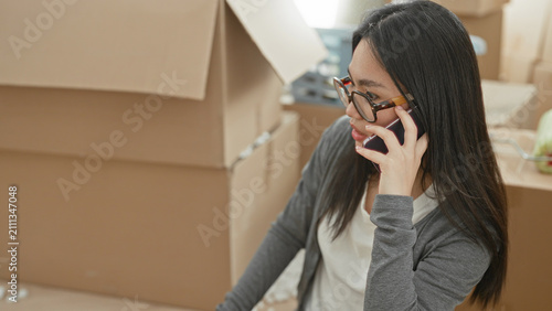 Foto Woman holding smartphone to ear and hand near face among stacked cardboard moving boxes in building; concern