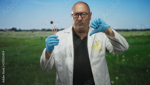 Bild auf Leinwand Man dentist holding dental mirror and probes with gloved hands, thumbs down gesture in forest; professional disapproval