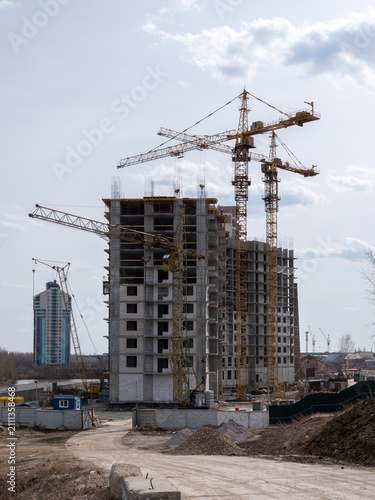 Construction site with tower cranes and high-rise building under development against a clear sky, urban architecture and building industry