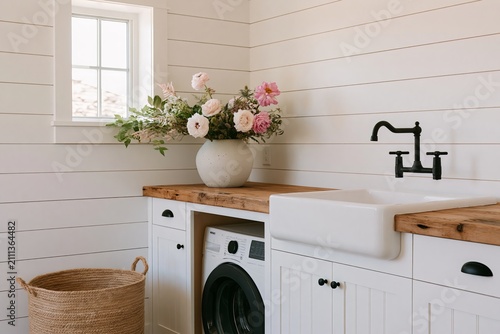 Modern farmhouse laundry room featuring white shiplap walls, a large sink, washing machine, wooden countertop, and a vase of flowers on display