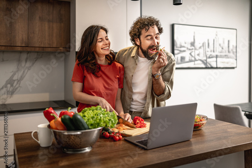 Happy couple cooking a healthy meal together in a modern kitchen while following an online recipe