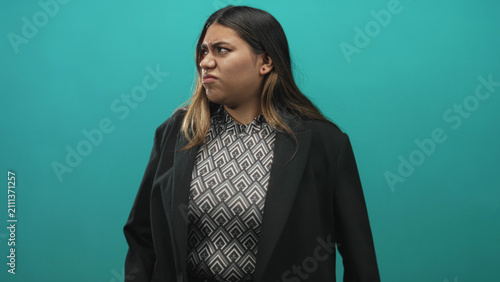 Foto Plus size woman grimaces with clenched fists and scrunched nose, wearing patterned blouse and black blazer in studio with teal backdrop; disgust rejection