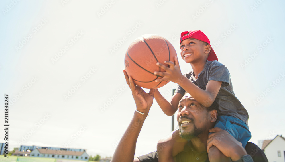Fototapeta premium black father and young boy playing basketball on a court, teaching little player and spending time outdoors