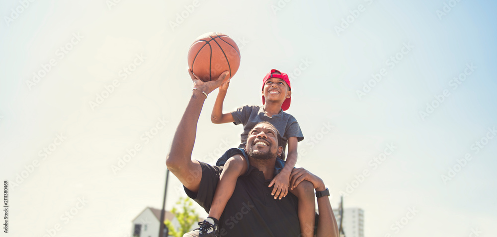 Fototapeta premium black father and young boy playing basketball on a court, teaching little player and spending time outdoors