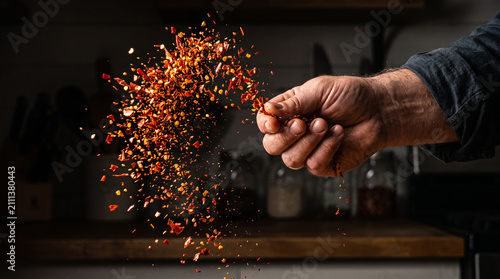 Hand tosses a handful of spicy red chili flakes into the air for seasoning.