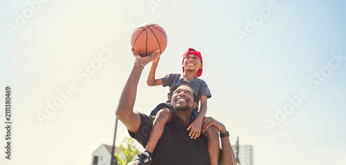 black father and young boy playing basketball on a court, teaching little player and spending time outdoors