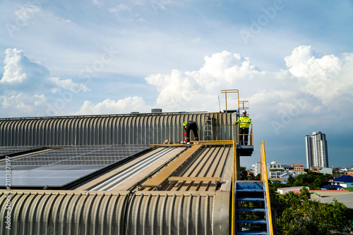 Workers install solar panels on a rooftop in the city during a bright day under a partly cloudy sky