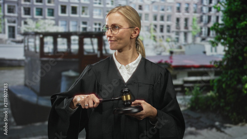 Фотография Woman judge in black robe holds gavel raised to strike in front of building; authority determination