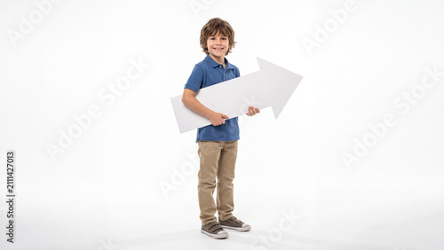 Schoolboy stands confidently while holding a large white directional arrow sign to indicate a path forward for academic or business marketing campaigns.
