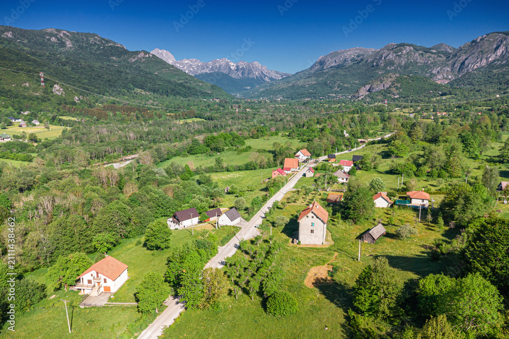 Obraz premium Aerial drone view of a small mountain village road winding through green valley. Travel concept.