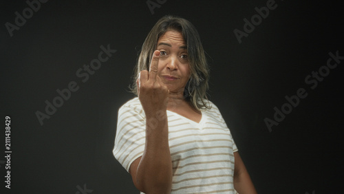Photography Hispanic woman shows middle finger with left hand while clenching right fist in studio; defiance provocation